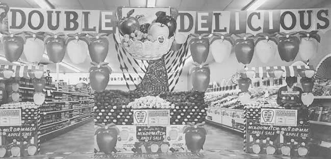 1960 年代杂货店的黑白照片 Double Delicious 苹果展示架，上面有气球和彩带